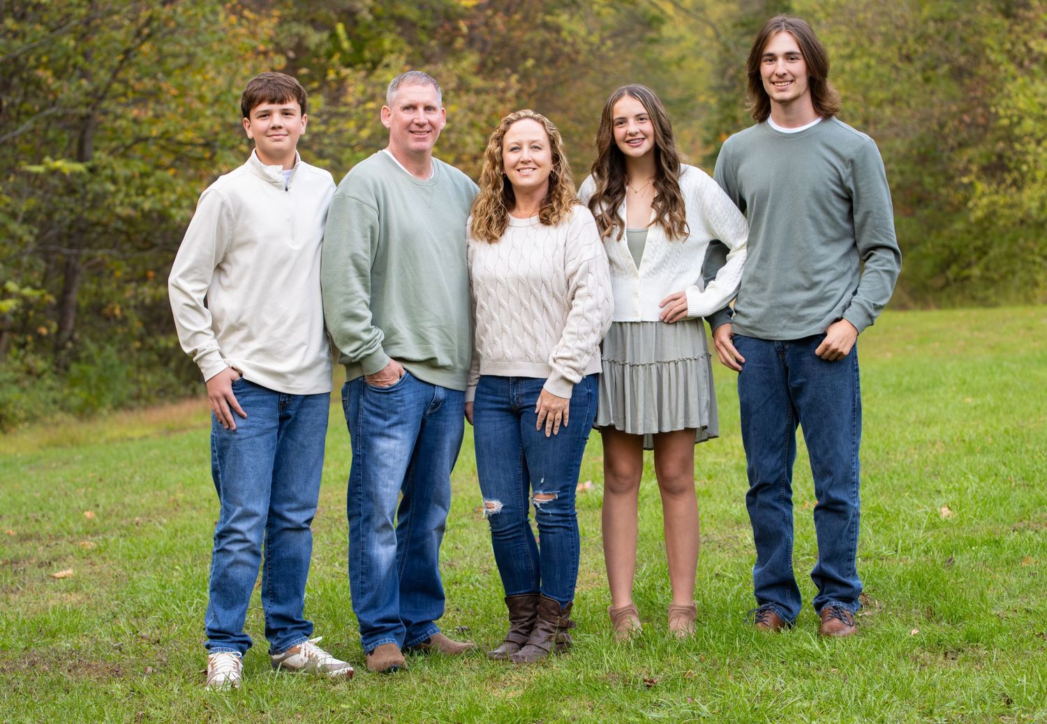 Family of five smiling together in a green autumn meadow for an outdoor portrait.