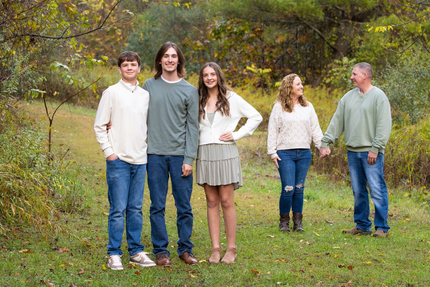 Family of five posing casually in an autumn field with colorful foliage backdrop.