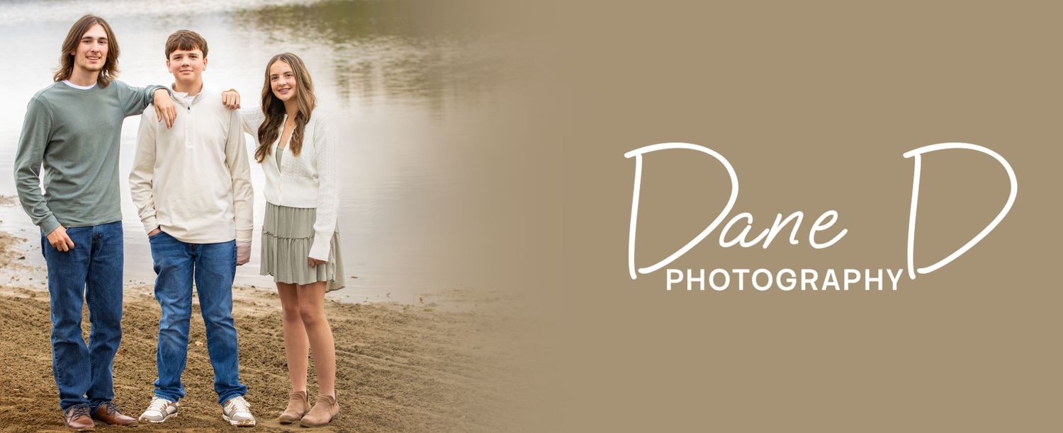 Three siblings smiling together on a lakeside path, Dane D Photography family portrait.