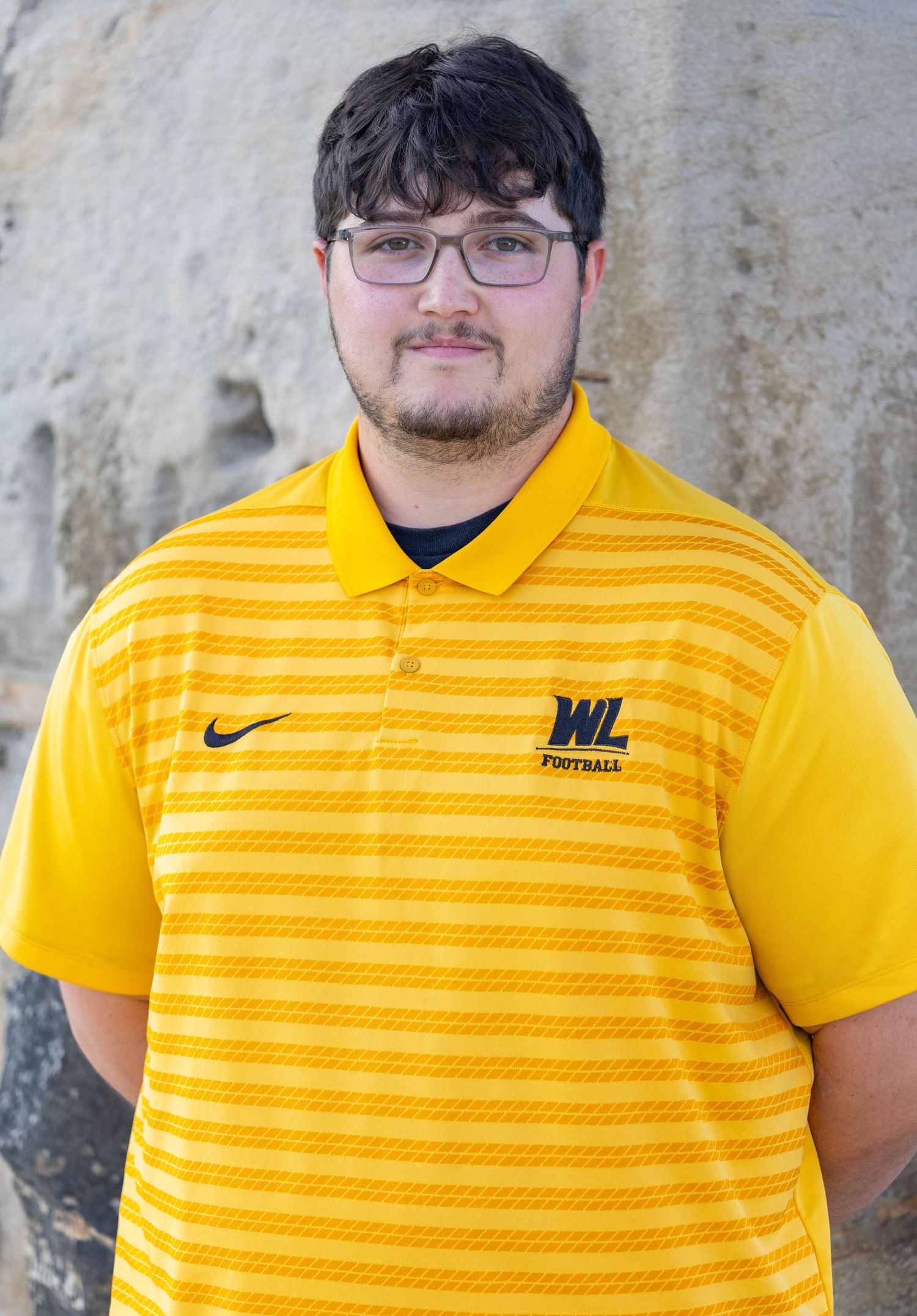 Young man in yellow polo shirt posing for a portrait photo outdoors.