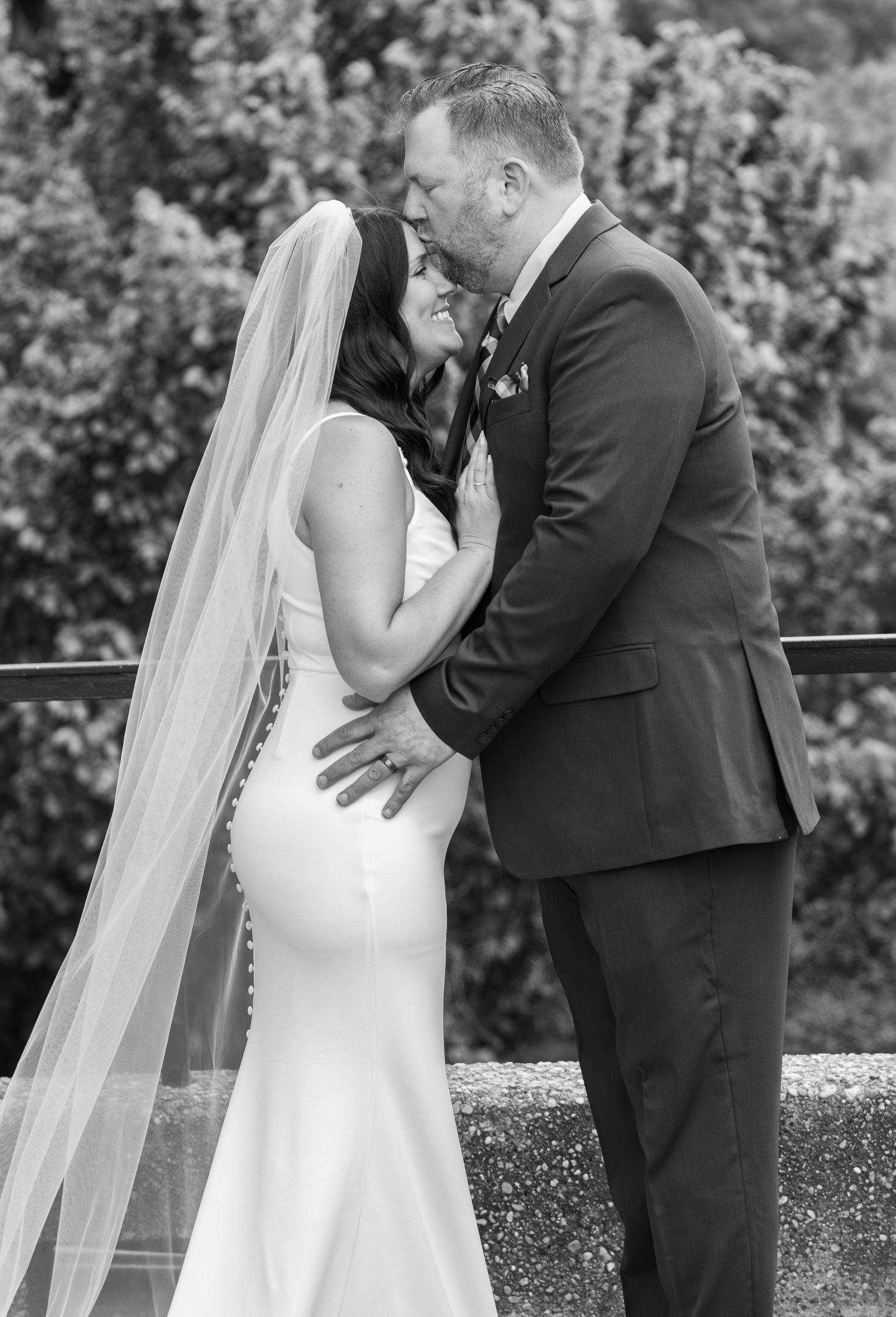 Black and white photo of bride and groom embracing and kissing outdoors.