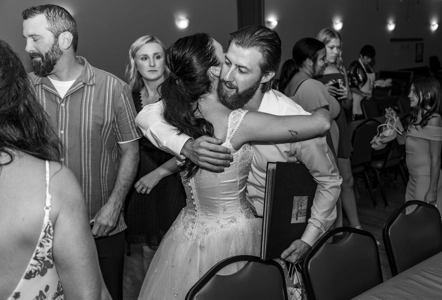 Black and white photo of bride and groom sharing a hug at wedding dinner.