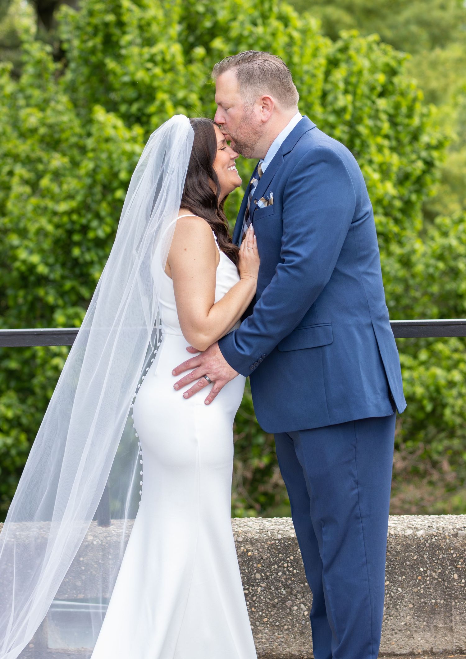 Newlyweds sharing romantic kiss outdoors with lush green garden background.