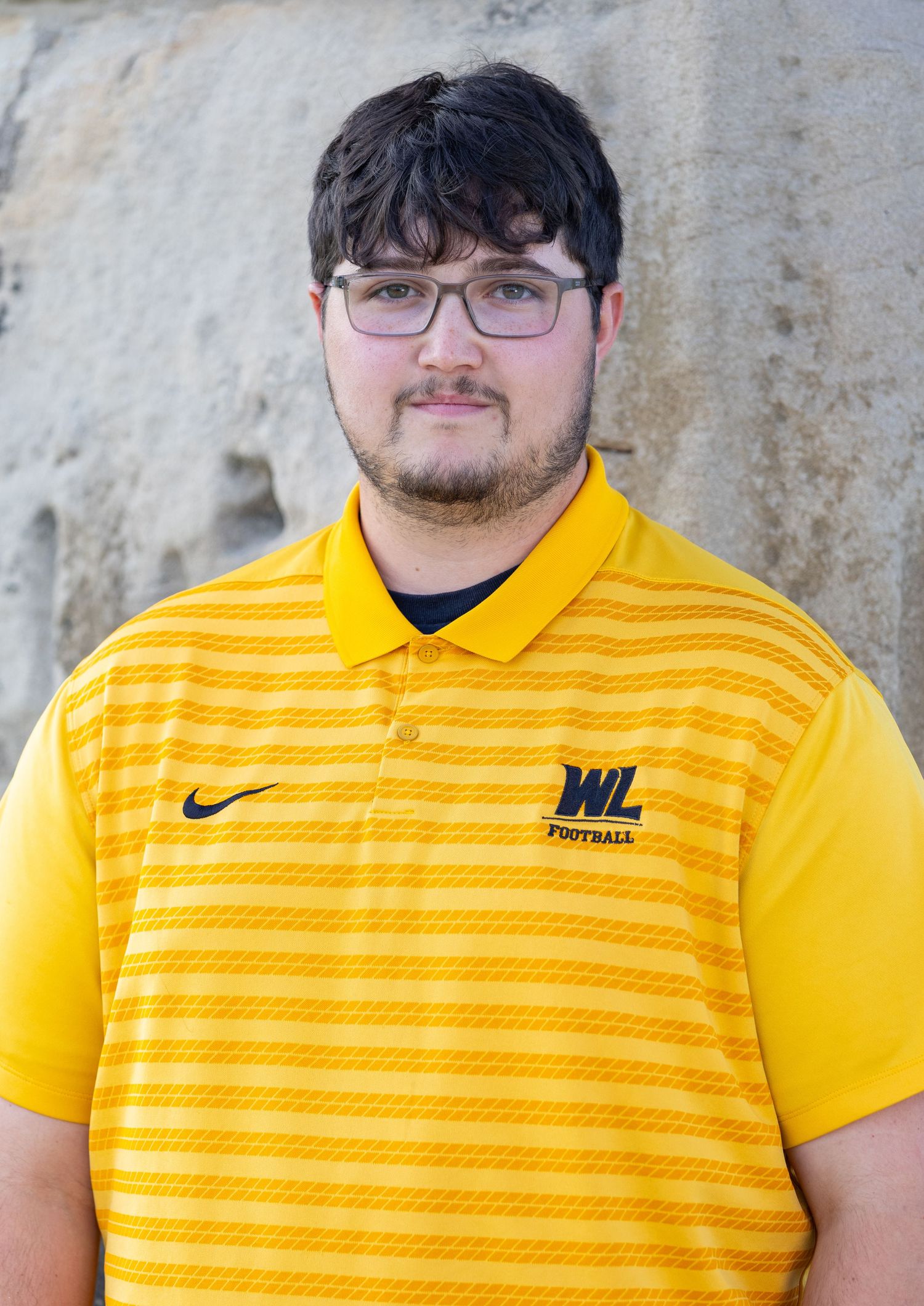 Young man wearing yellow polo shirt posing against stone wall background.