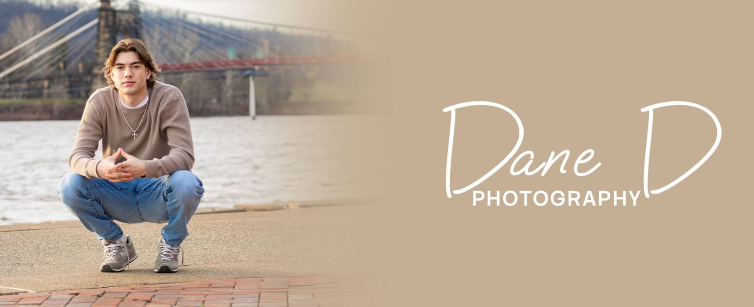 Young man in casual hoodie crouching near waterfront bridge, Dane D Photography senior portrait.