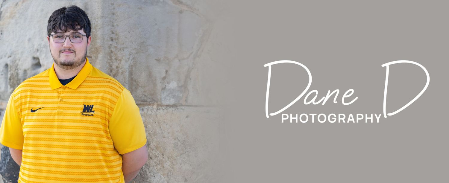 Young man in yellow polo shirt posing against stone wall, Dane D Photography.