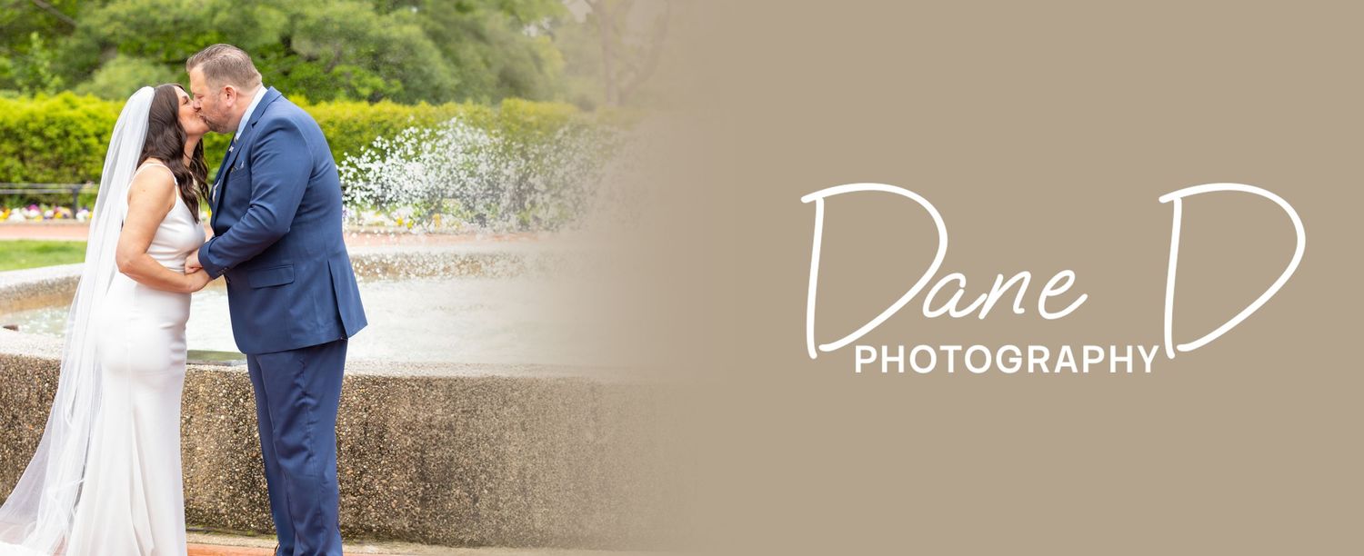 Couple in wedding attire sharing tender moment by outdoor fountain, Dane D Photography.