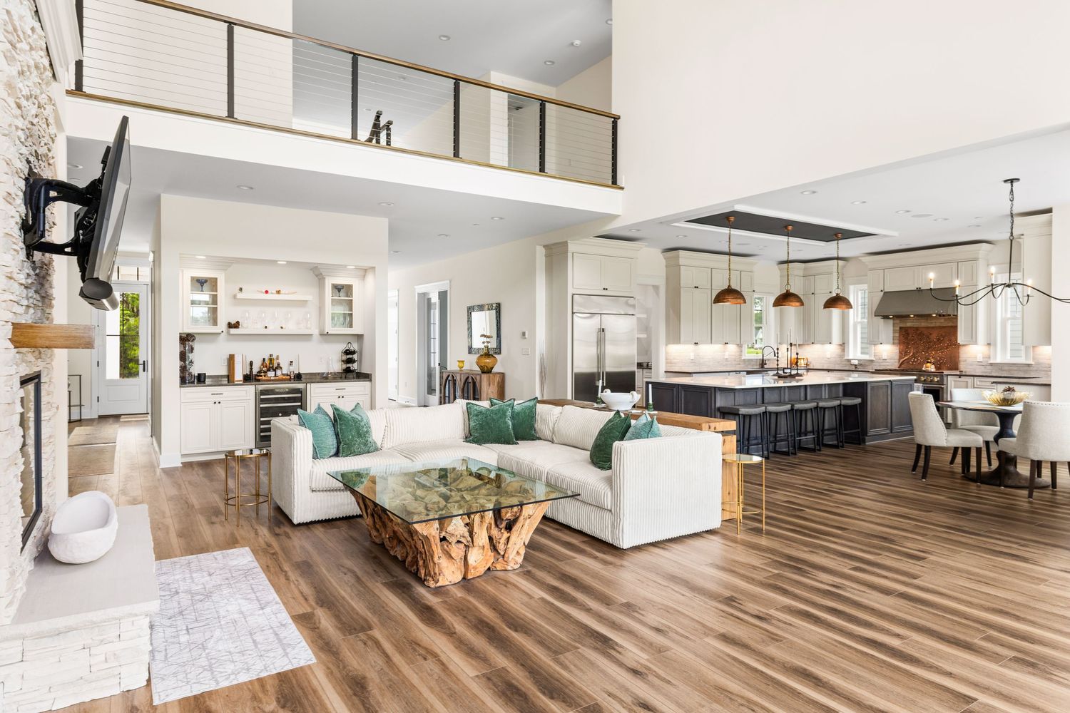 Open-concept living room with white sectional, wood coffee table, hardwood floors, kitchen island, and soaring two-story ceilings.