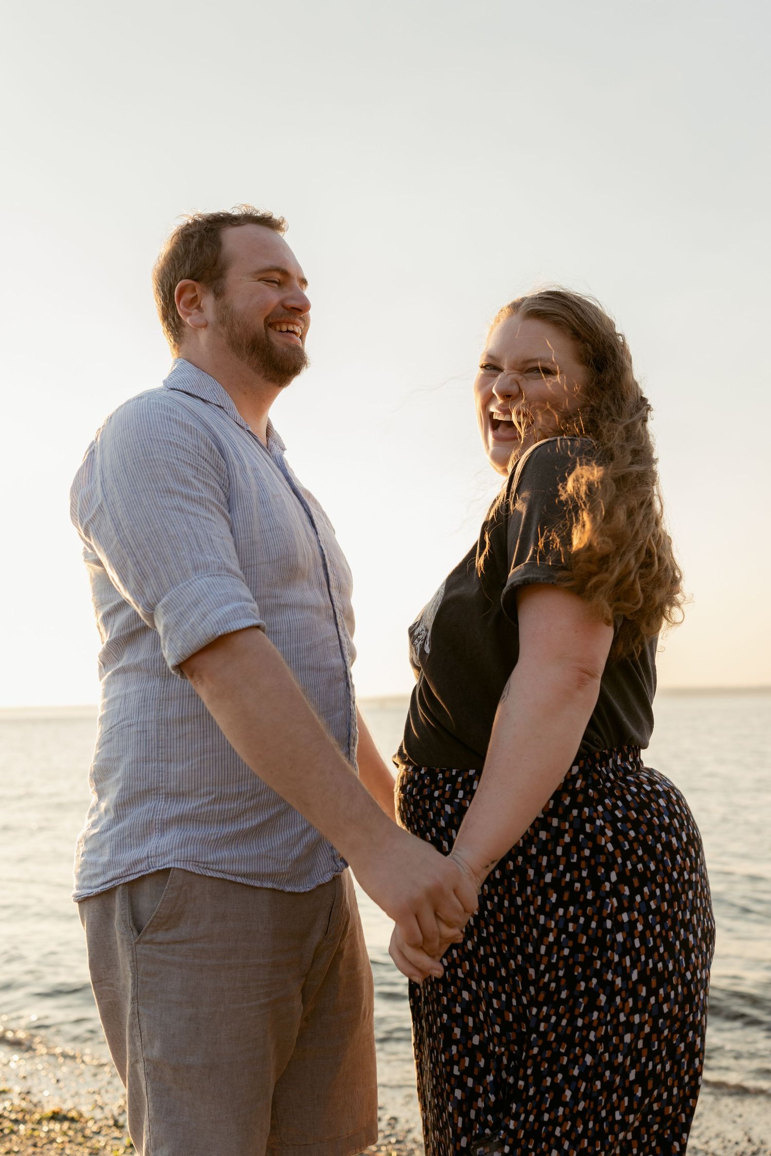 Couple holding hands and looking toward the camera during an outdoor portrait session at Golden Gardens Beach in Seattle.