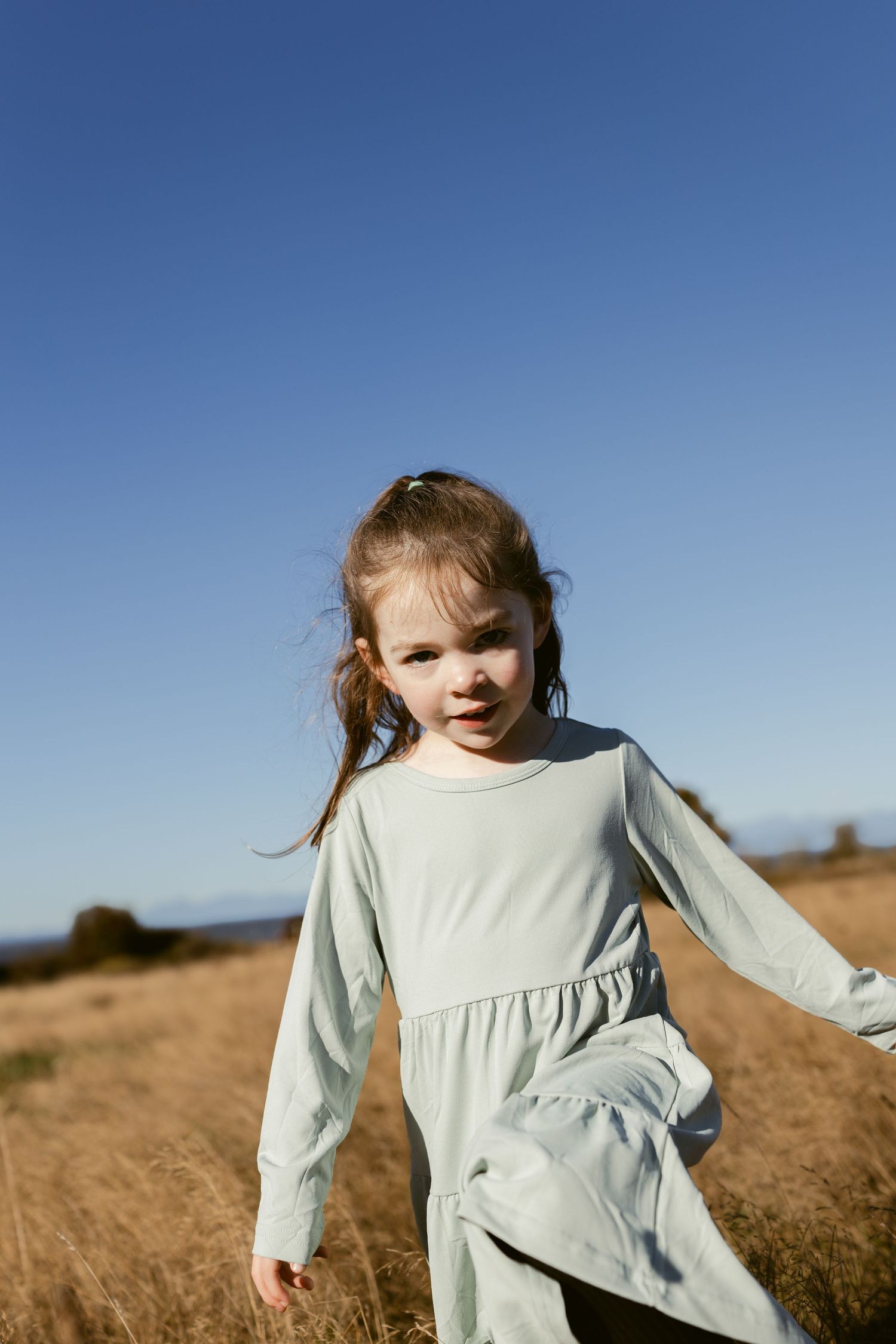 Young girl in a light blue dress walking through golden grass at Discovery Park in Seattle during a family photoshoot.