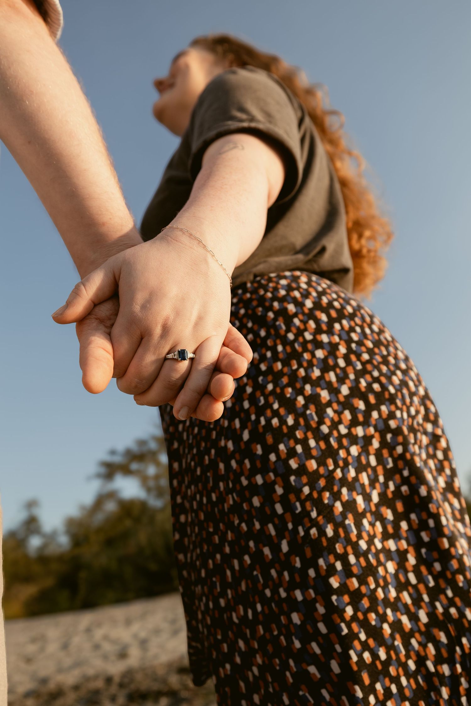 Low-angle candid portrait of a woman in a patterned dress holding her partner's hand during a couples photoshoot in Seattle.