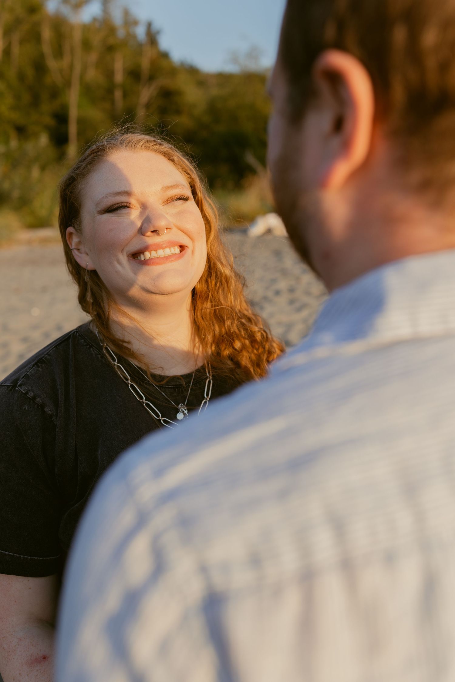 Woman smiling at her partner during a candid couples photoshoot at Golden Gardens Beach in Seattle, with warm sunset light.