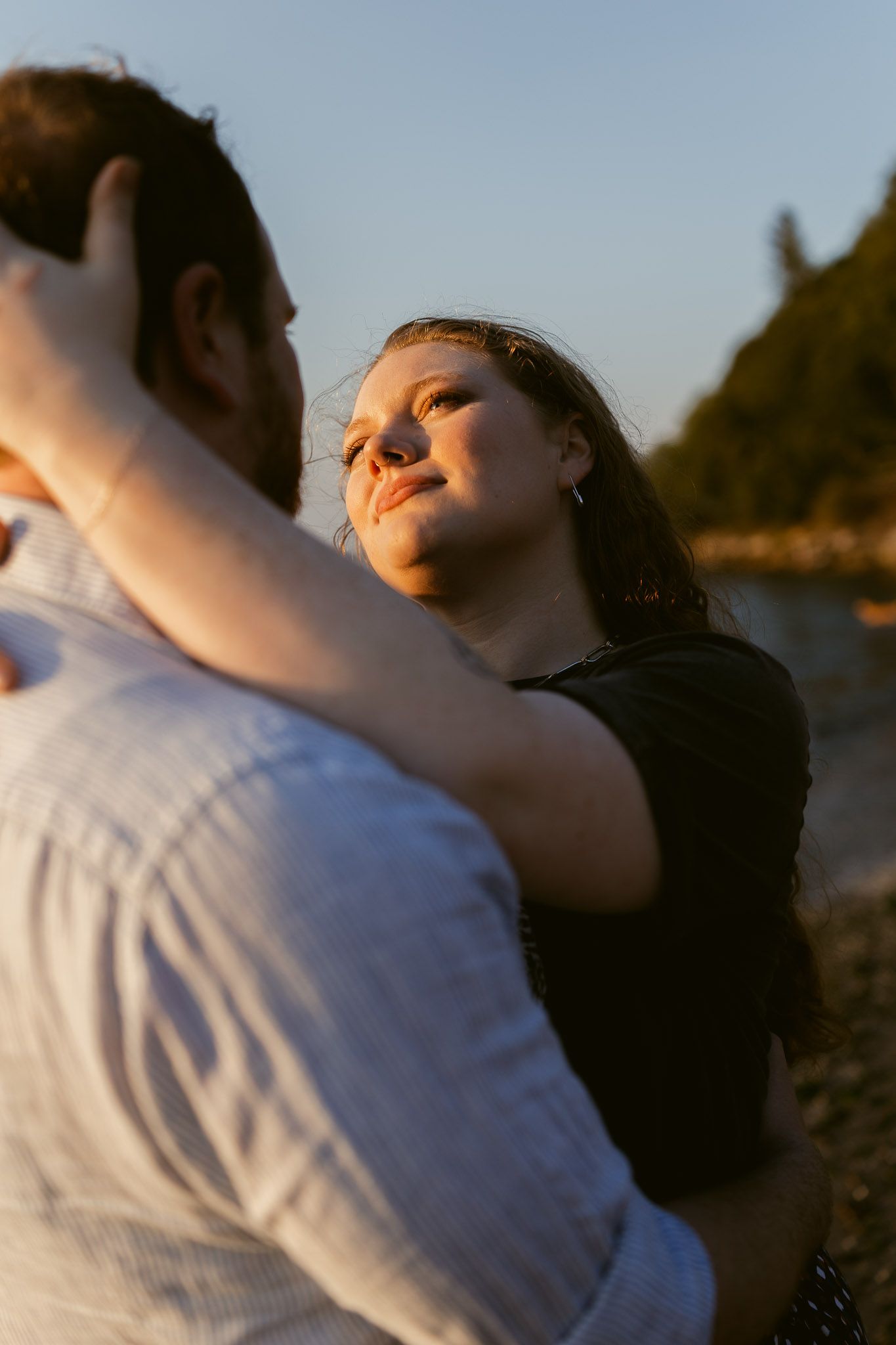 Candid couples portrait at Golden Gardens Beach in Seattle, with a woman smiling at her partner in warm evening light.