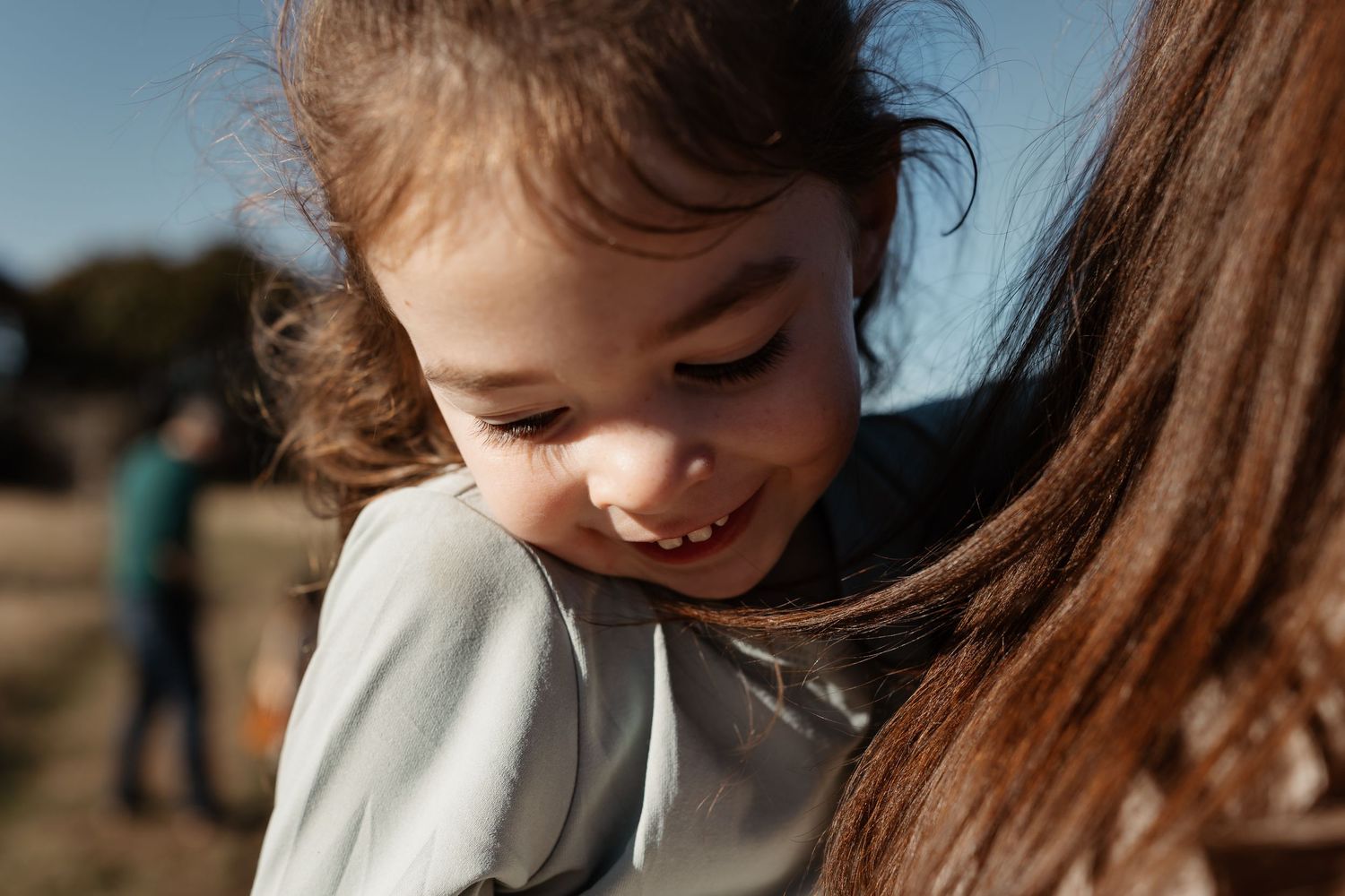 Candid close-up of a young girl smiling while hugging a family member outdoors at Discovery Park in Seattle.