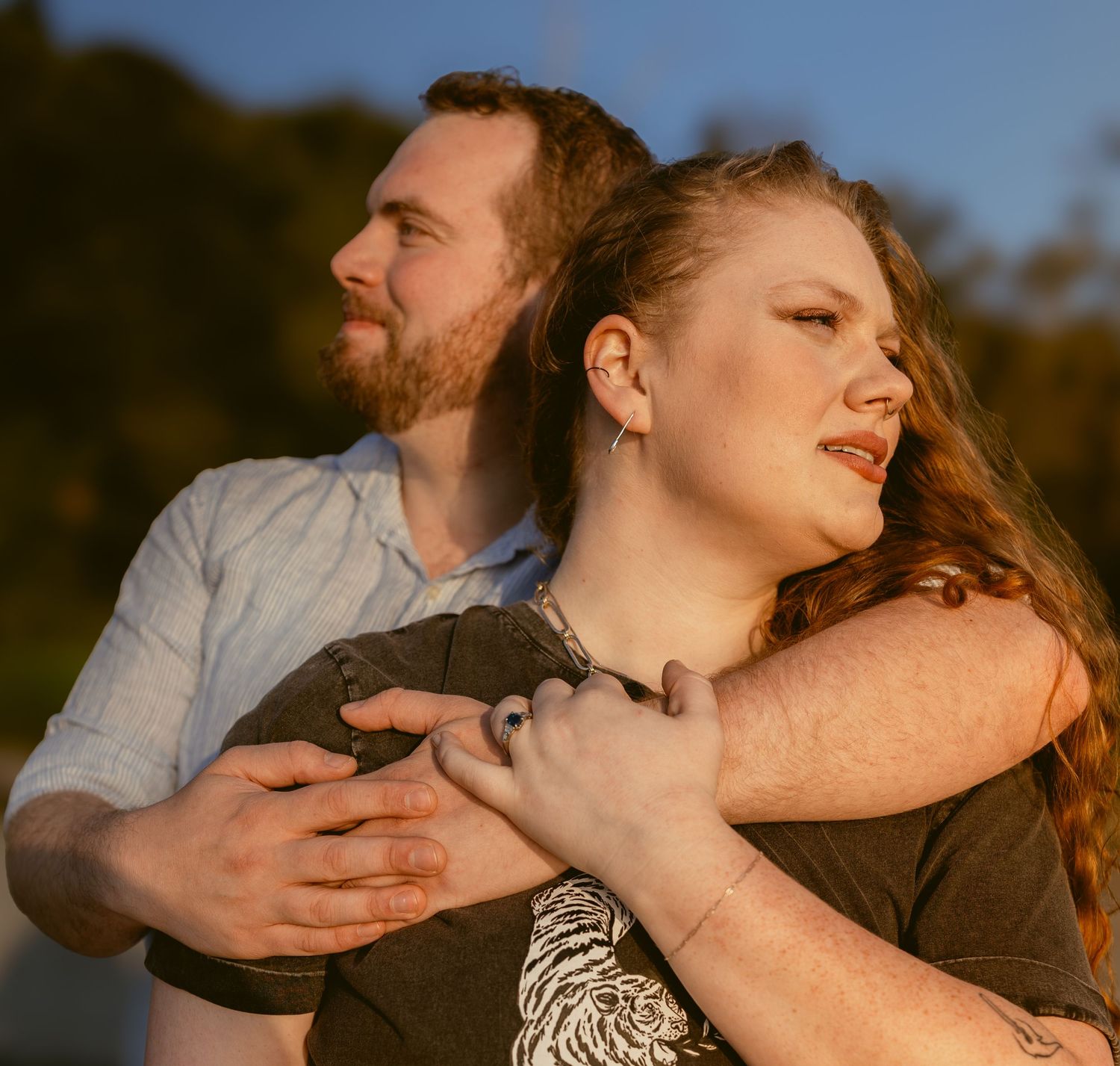 Candid couples portrait of a man embracing his partner from behind in warm evening light at Golden Gardens Beach in Seattle.