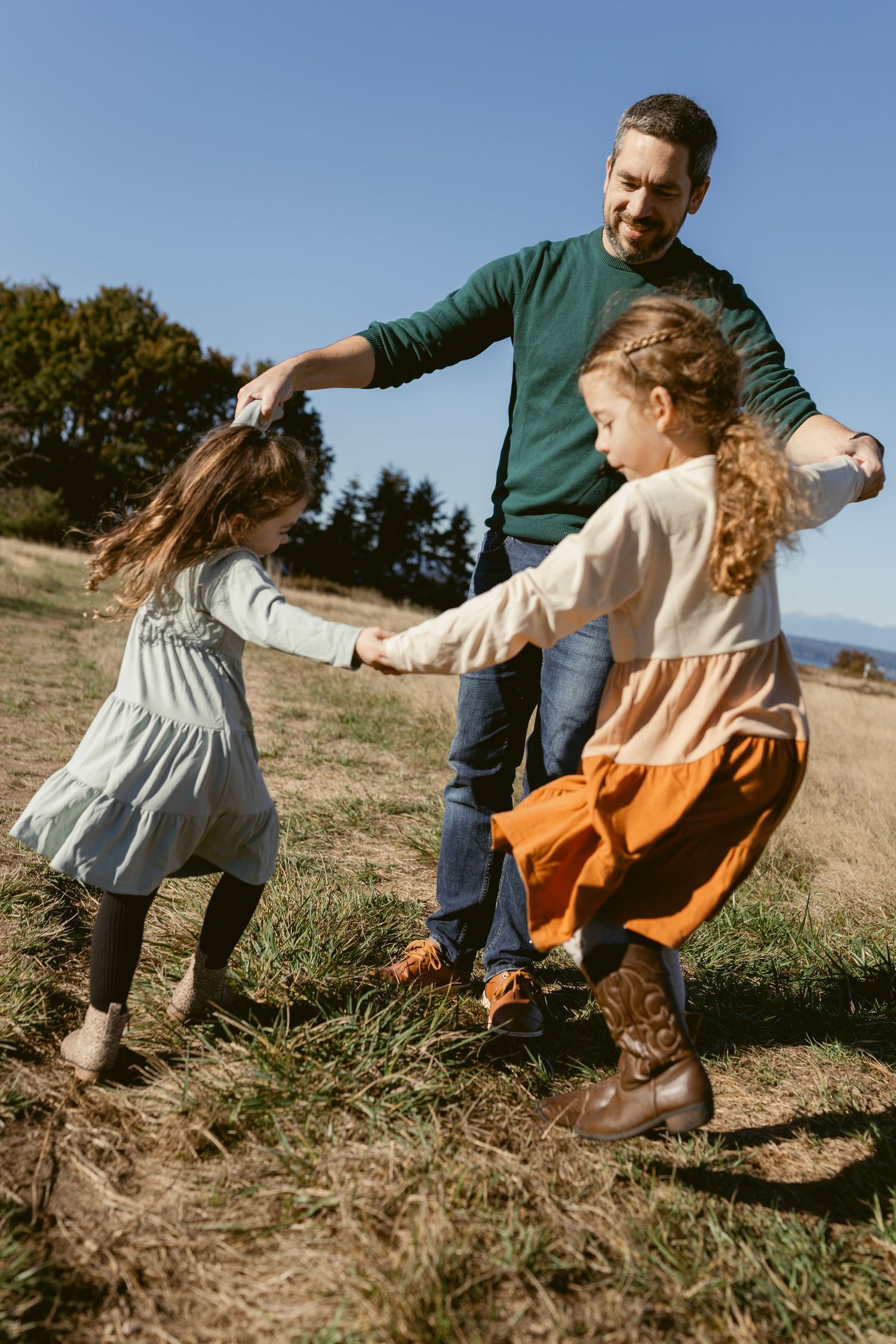 Father playing with his two young daughters in a grassy field at Discovery Park in Seattle during an outdoor family photoshoot.