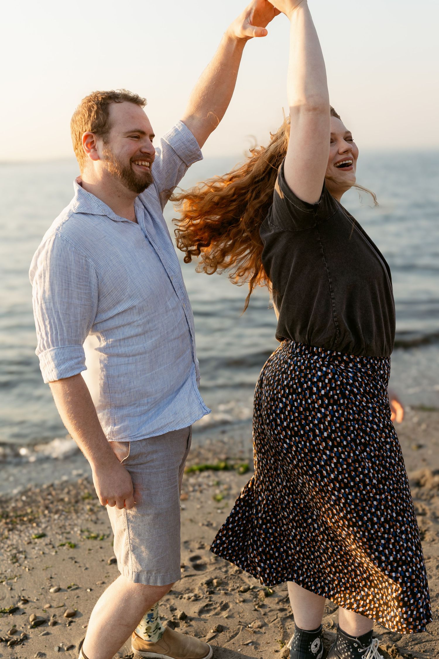 Couple dancing together on the beach at Golden Gardens in Seattle, with the woman twirling beneath her partner's hand.