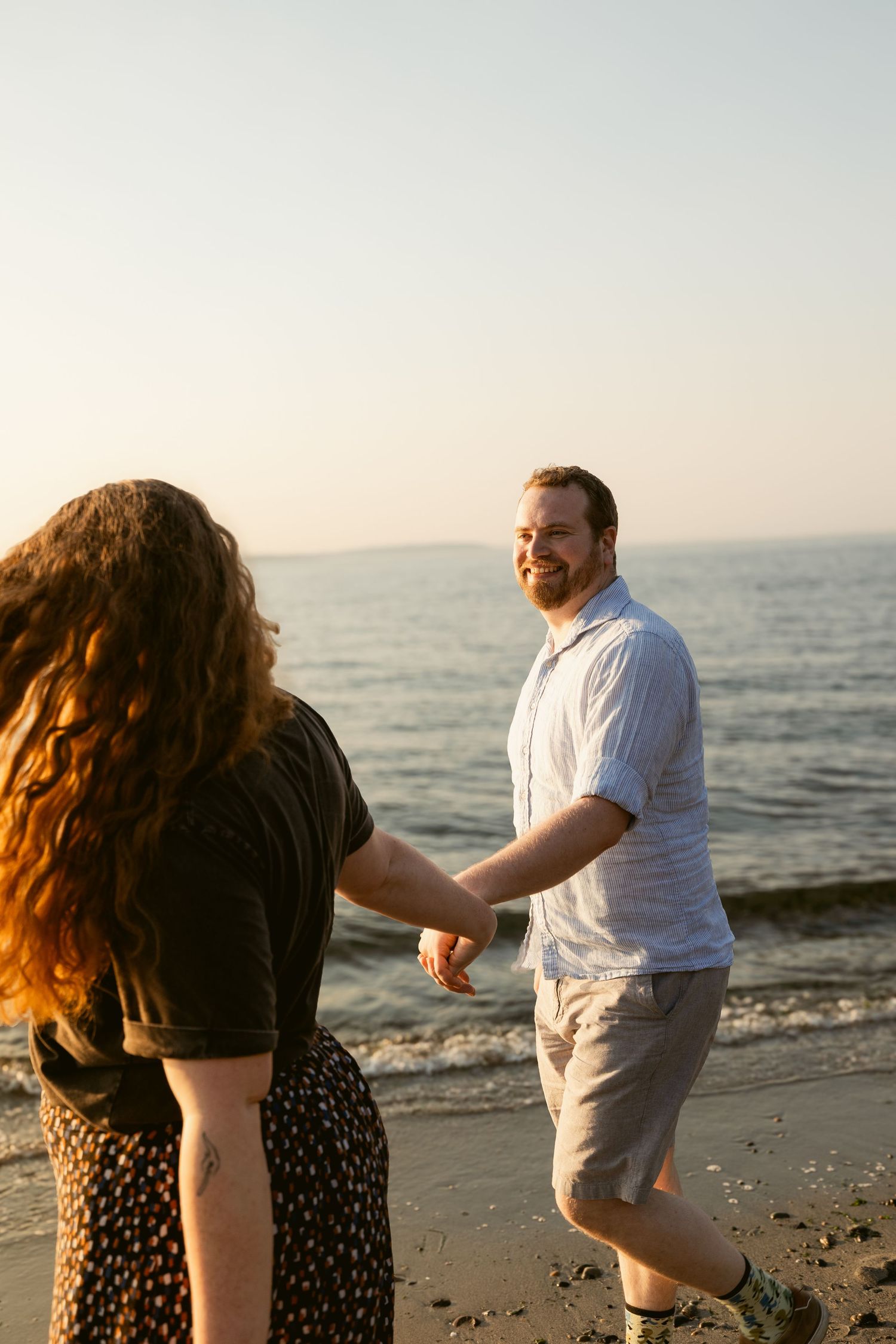 Couple holding hands along the shoreline at Golden Gardens Beach in Seattle during a sunset photoshoot.