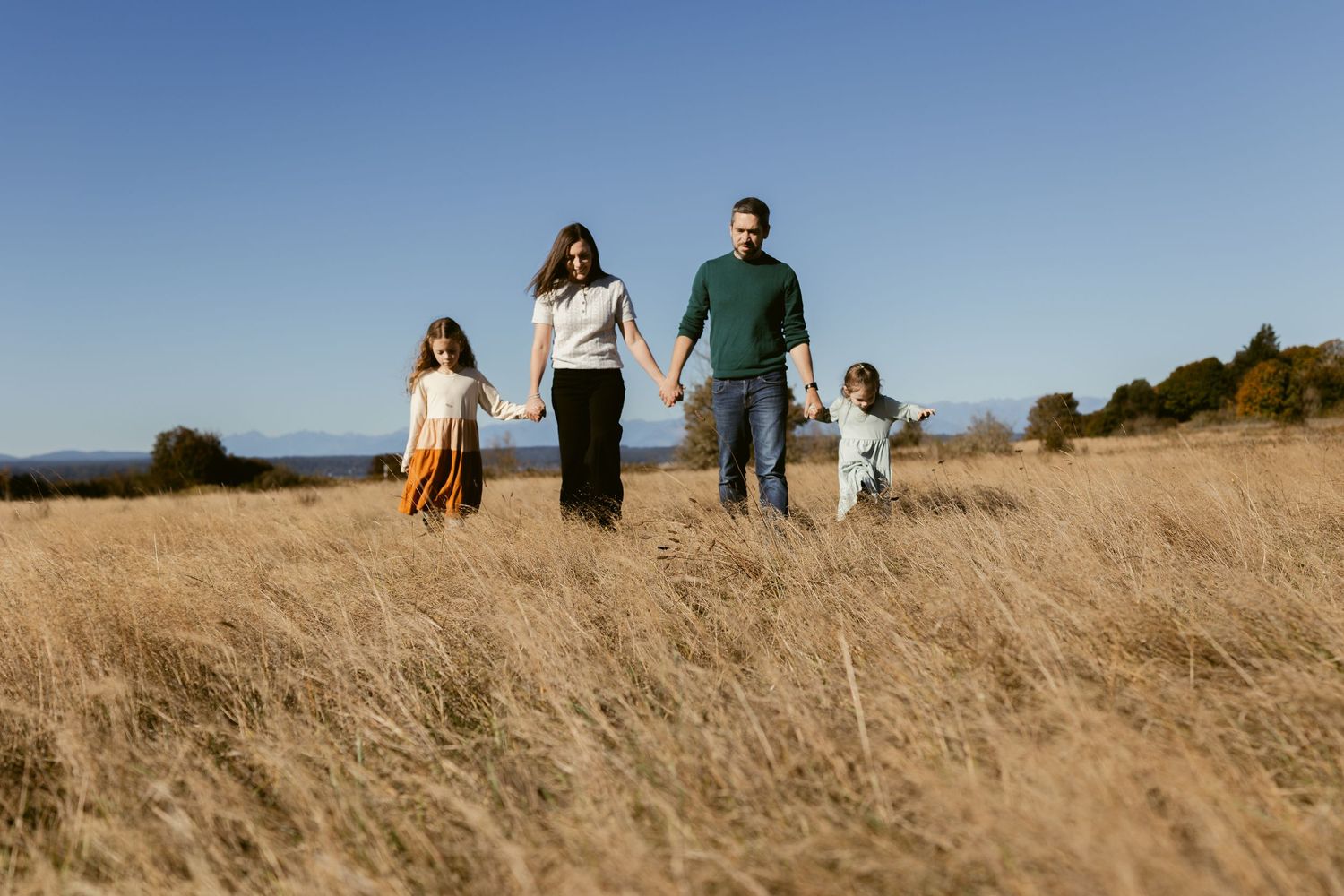 Family of four walking hand in hand through golden grass at Discovery Park in Seattle during an outdoor family photography session.