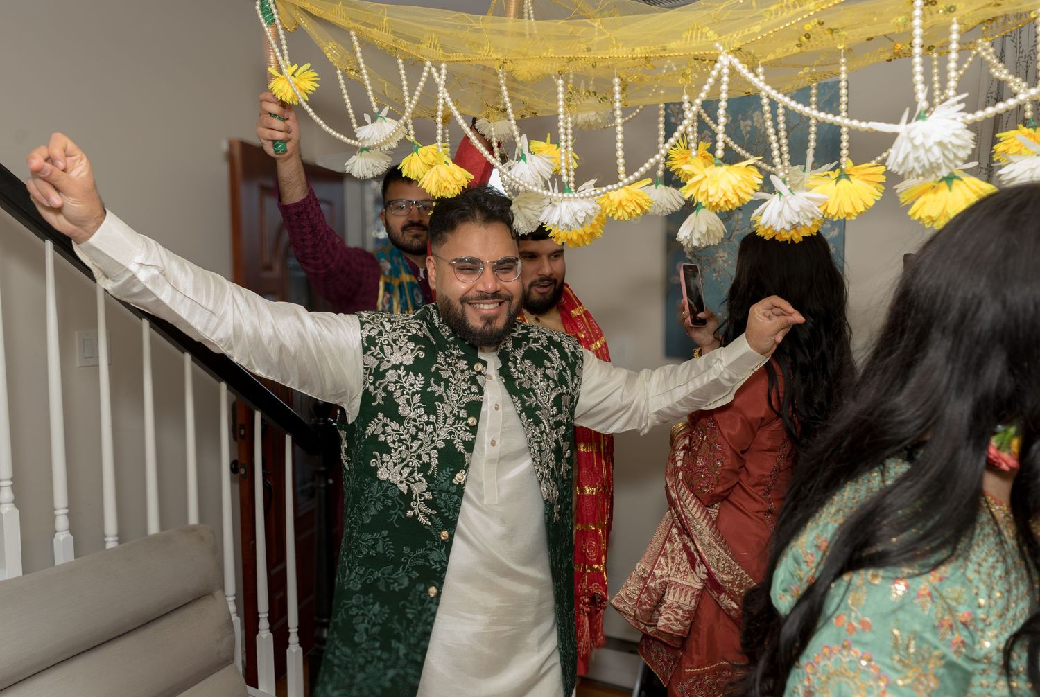 Groom in green sherwani celebrating joyfully with raised arms during South Asian wedding entrance.