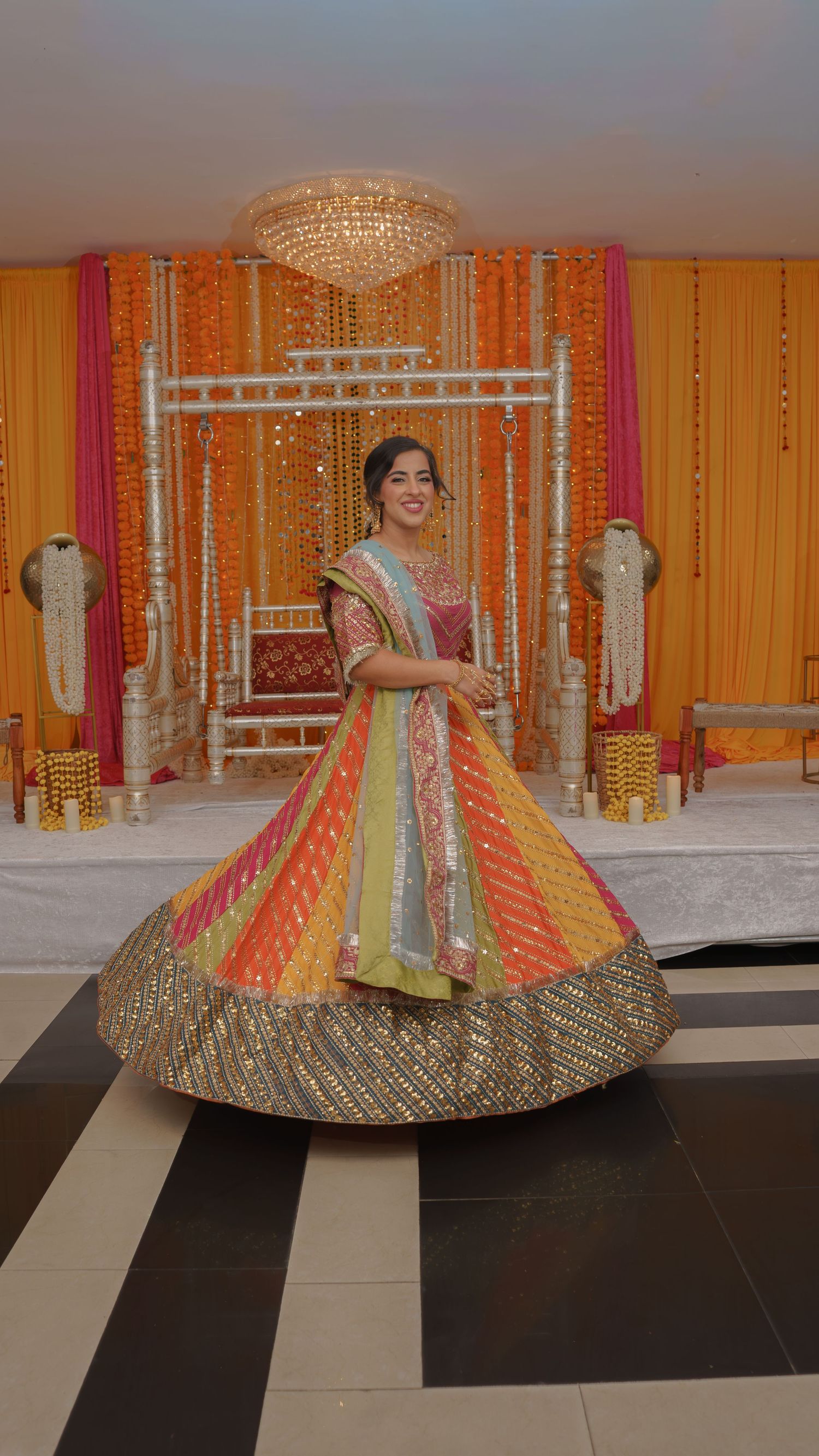 Bride twirling in vibrant multicolored lehenga at traditional South Asian mehndi celebration venue.