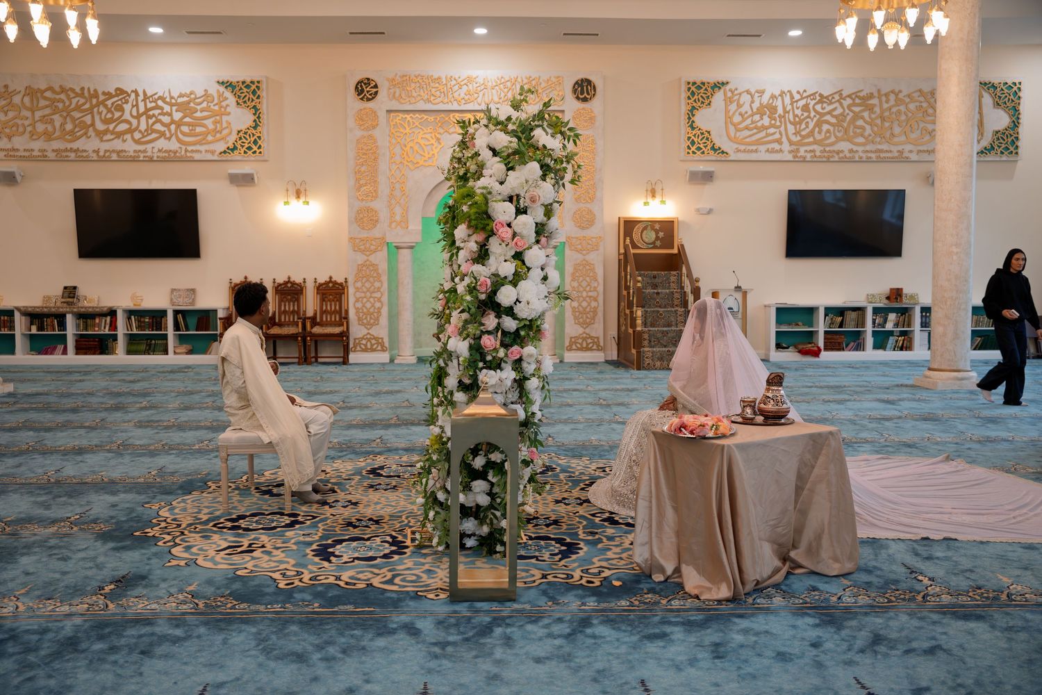 Elegant mosque interior with floral arch, decorated table, and blue carpet for a wedding ceremony.