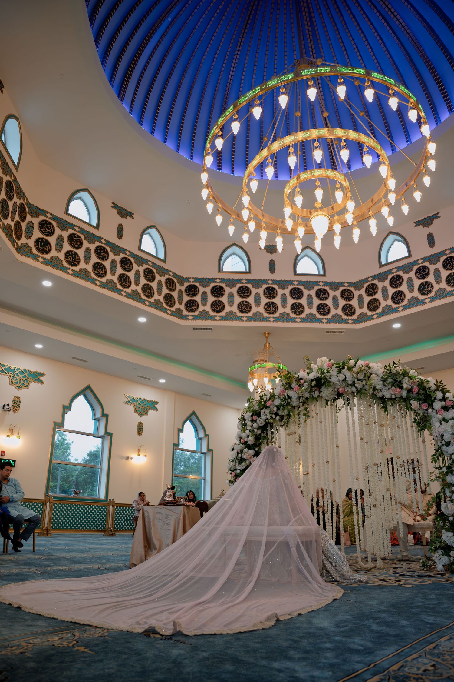 Elegant wedding venue interior with ornate dome ceiling, chandeliers, and floral bridal arch centerpiece.