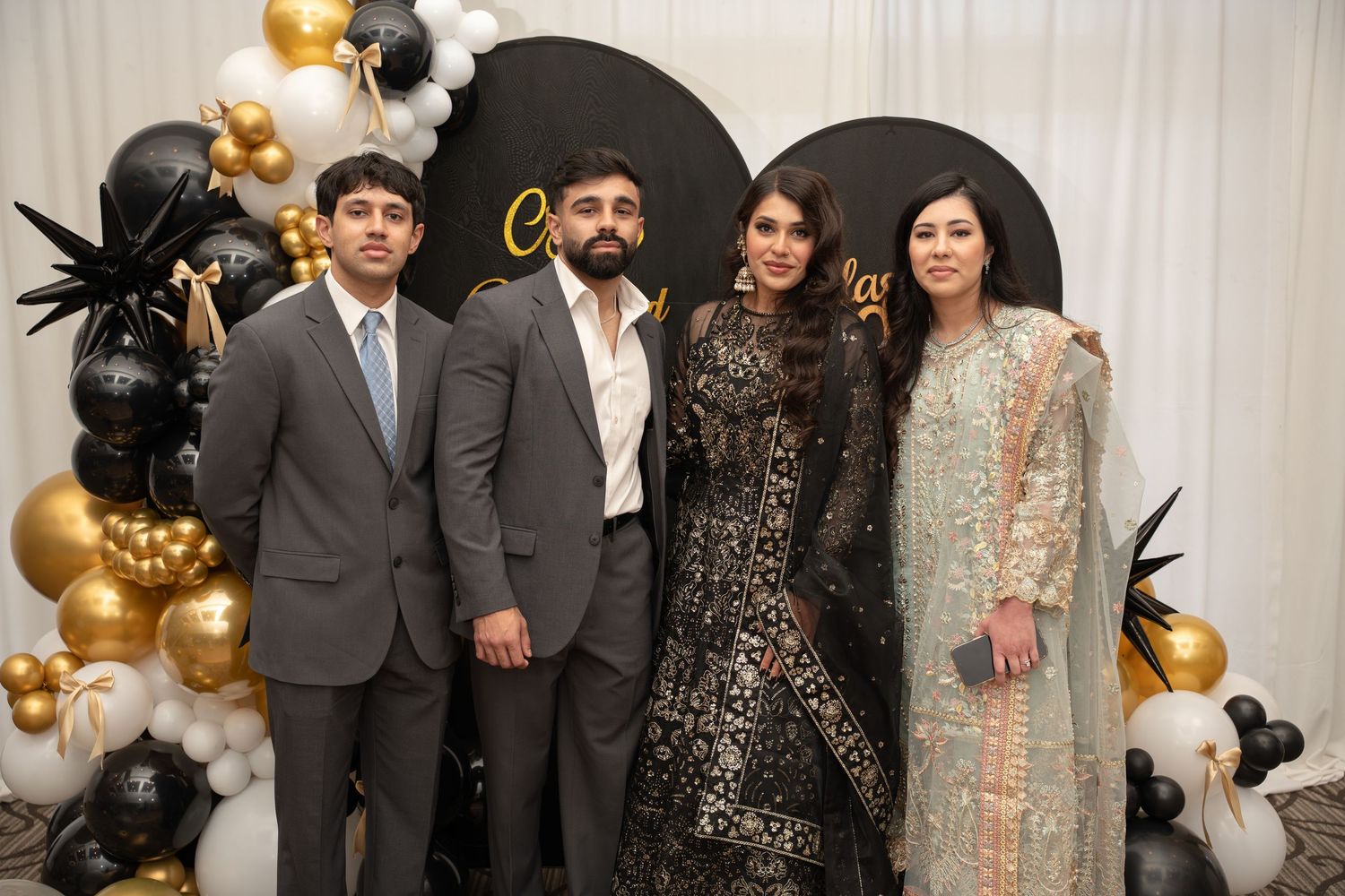 Family of four posing together at elegant black and gold celebration event with balloon decorations.