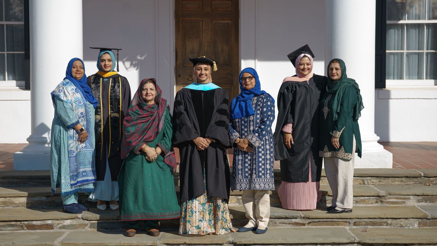 Group of graduates and guests posing on steps at academic graduation ceremony.