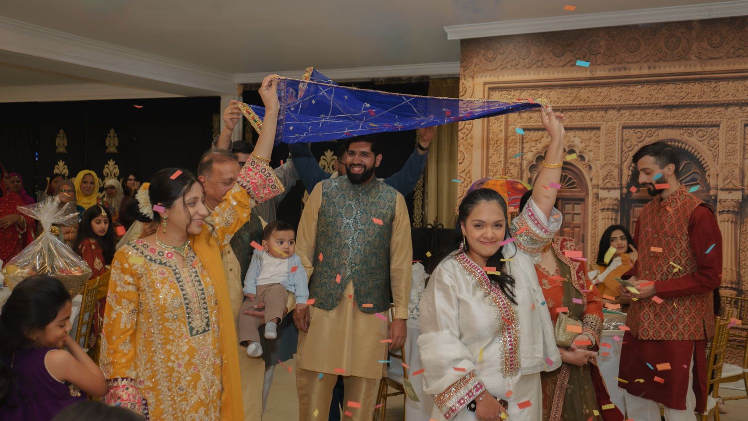 Group celebrating with blue dupatta at vibrant South Asian cultural wedding event.