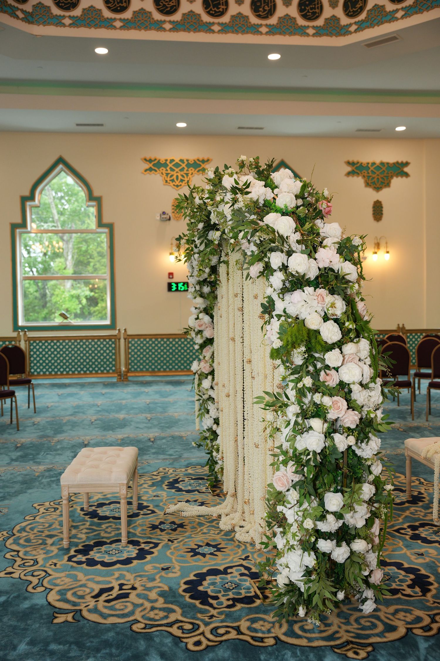 Elegant floral arch with white peonies and greenery in a decorated wedding venue with teal carpet.