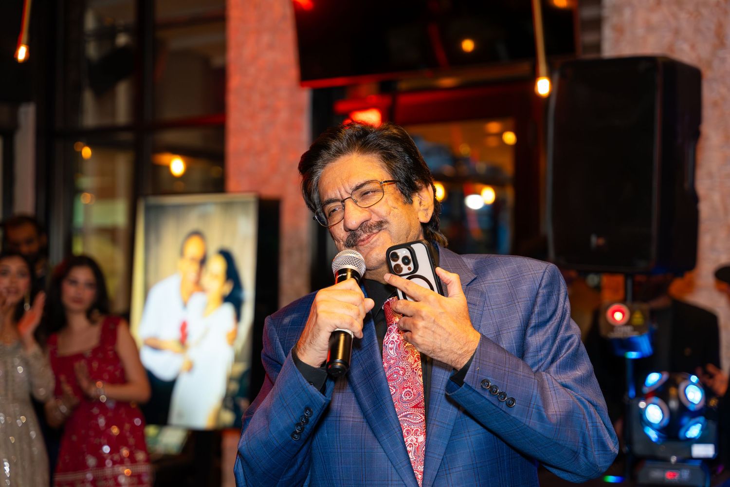 Man in blue blazer speaking into microphone at elegant indoor event.