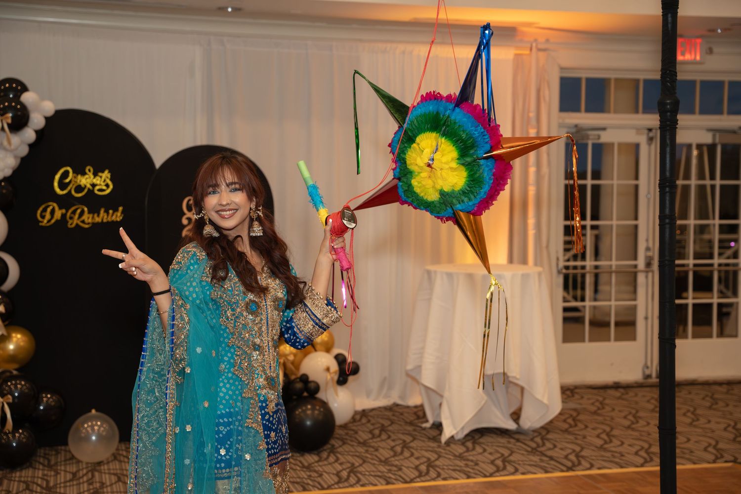 Woman in teal traditional South Asian attire posing with colorful star piñata at festive indoor celebration.