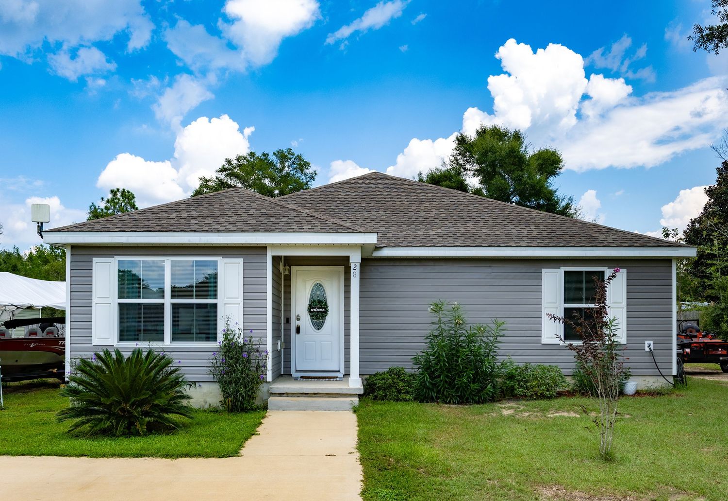 Gray vinyl-sided ranch home with white front door, covered entry, palm tree, and concrete walkway on a sunny day.