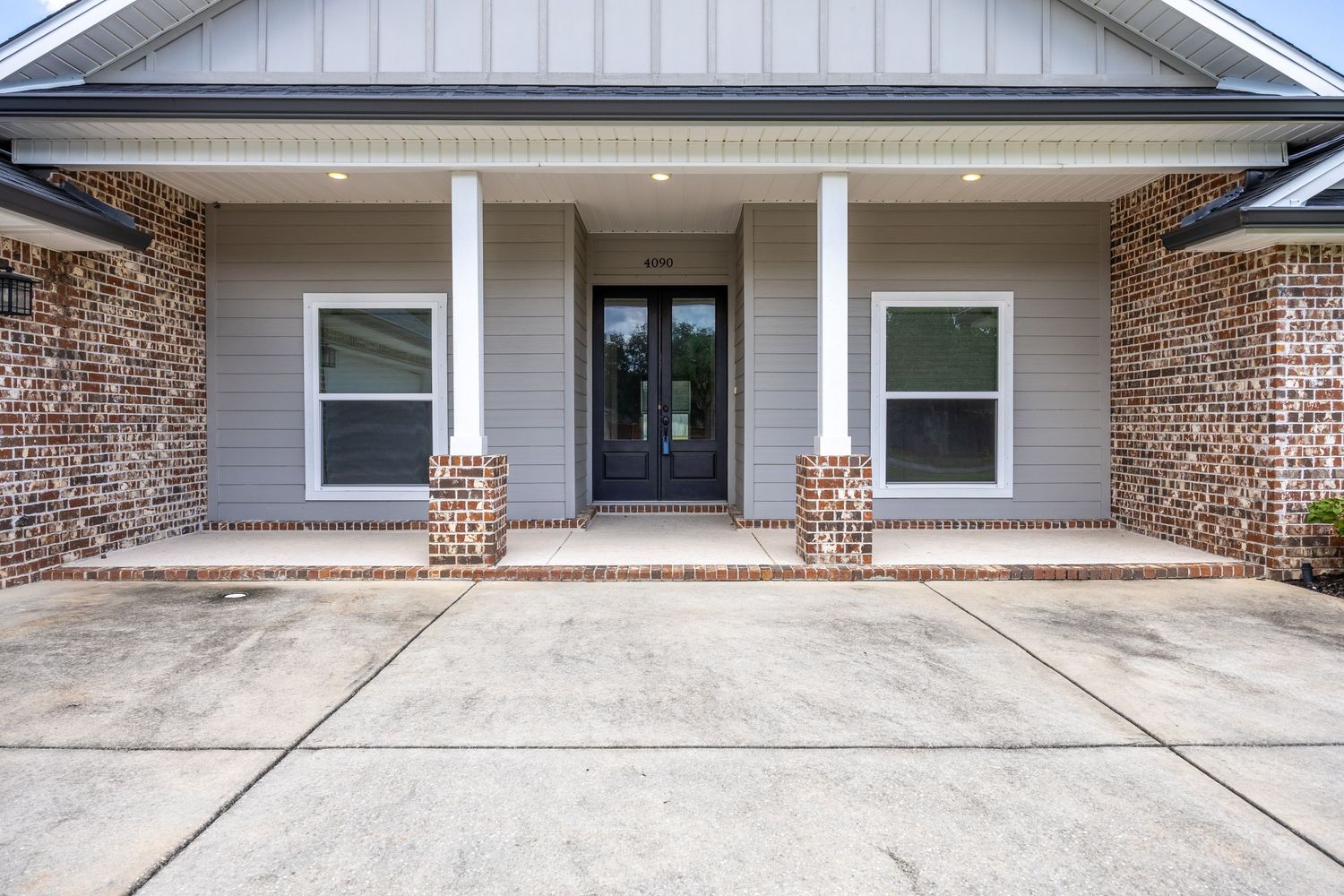 Brick and gray siding home exterior featuring a covered front porch with white columns and a black double entry door.