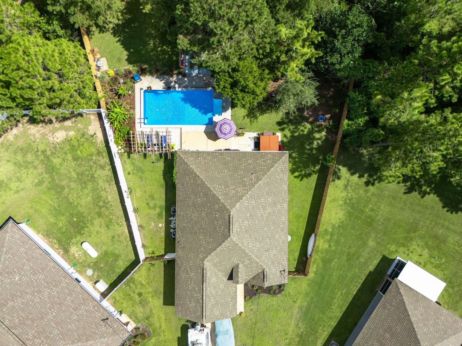 Aerial view of a suburban home with a gray roof surrounded by lush green lawn and a rectangular swimming pool.