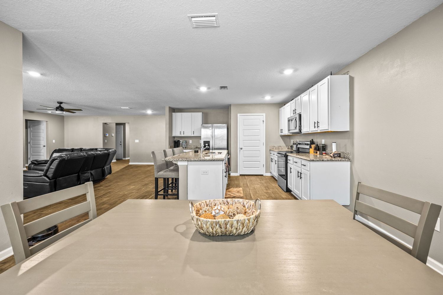Open-concept kitchen and living area with white cabinets, stainless appliances, hardwood floors, and dining table in foreground.