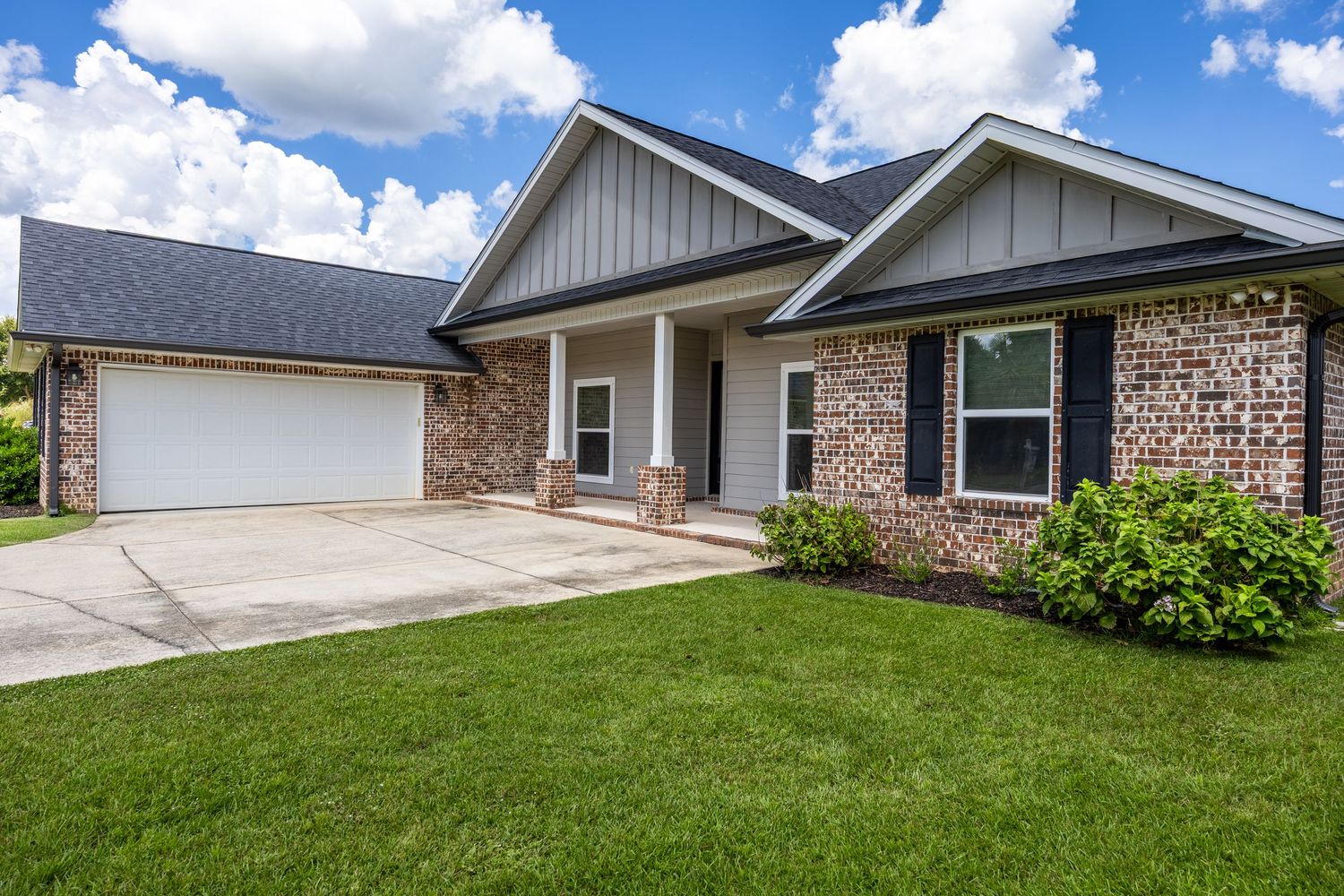 Craftsman-style brick and board-and-batten home with covered porch, attached garage, and well-maintained lawn.