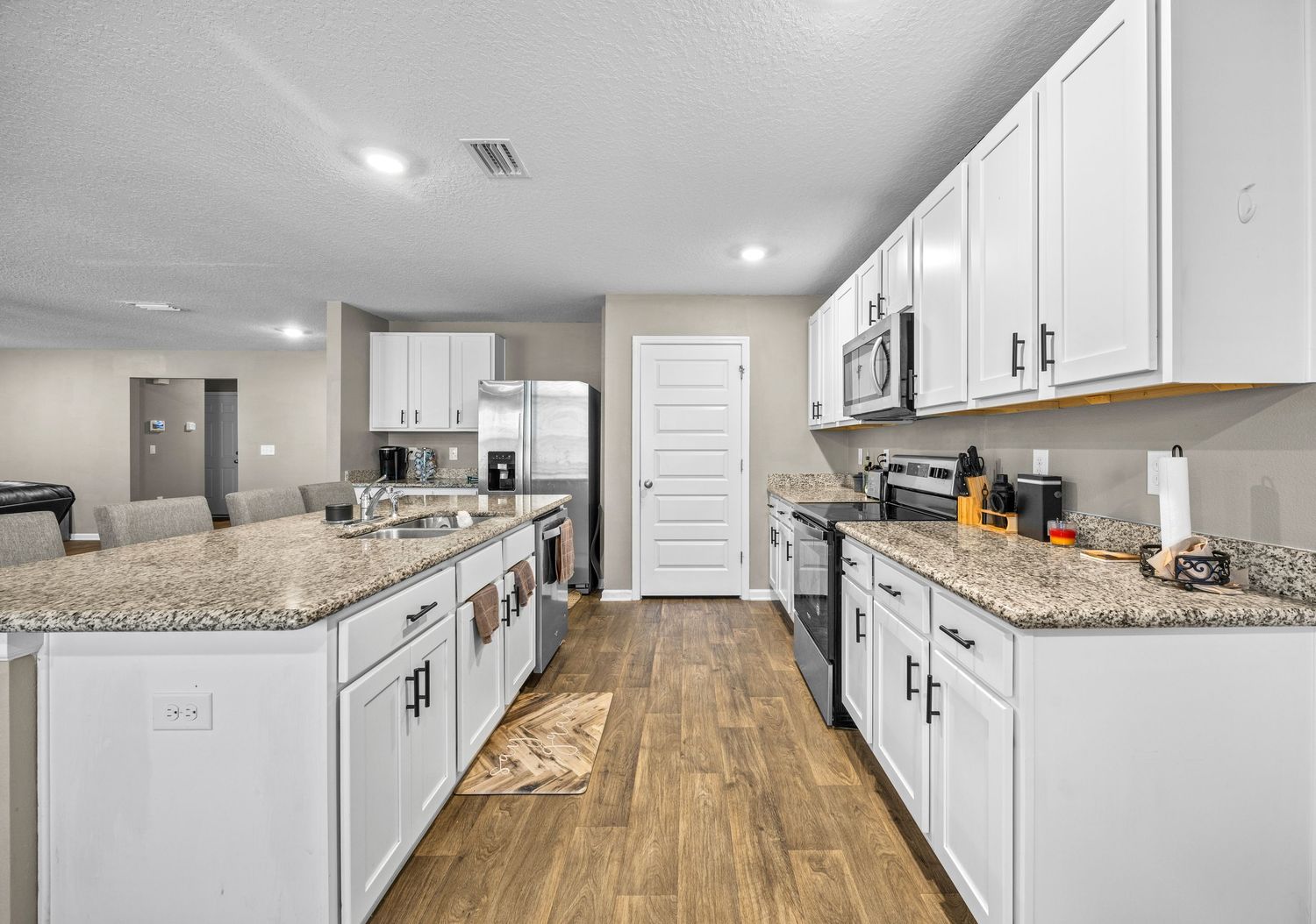 Modern kitchen with white cabinets, granite countertops, stainless steel appliances, and hardwood floors.