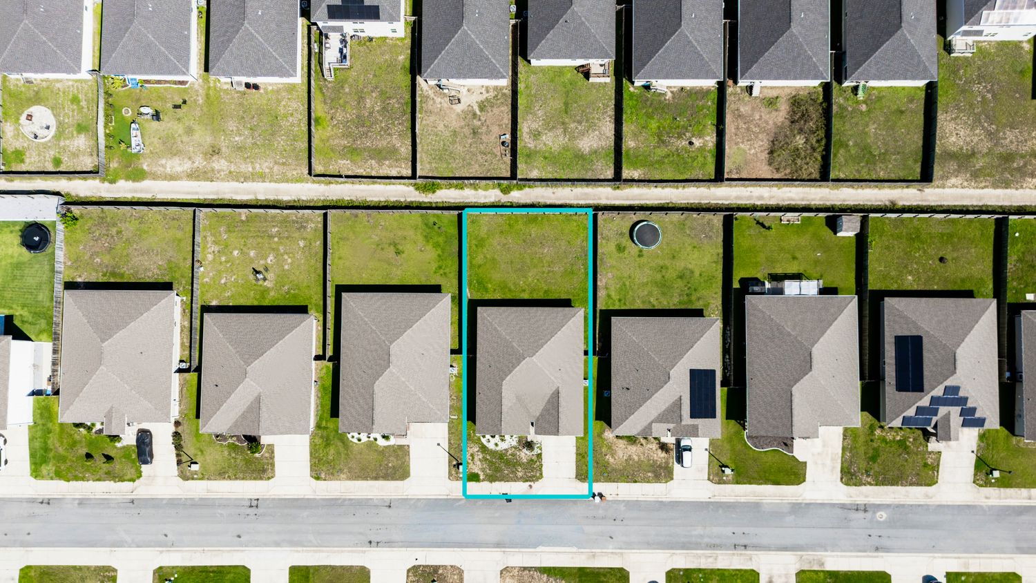 Aerial view of a vacant residential lot outlined in teal among suburban homes with green lawns.
