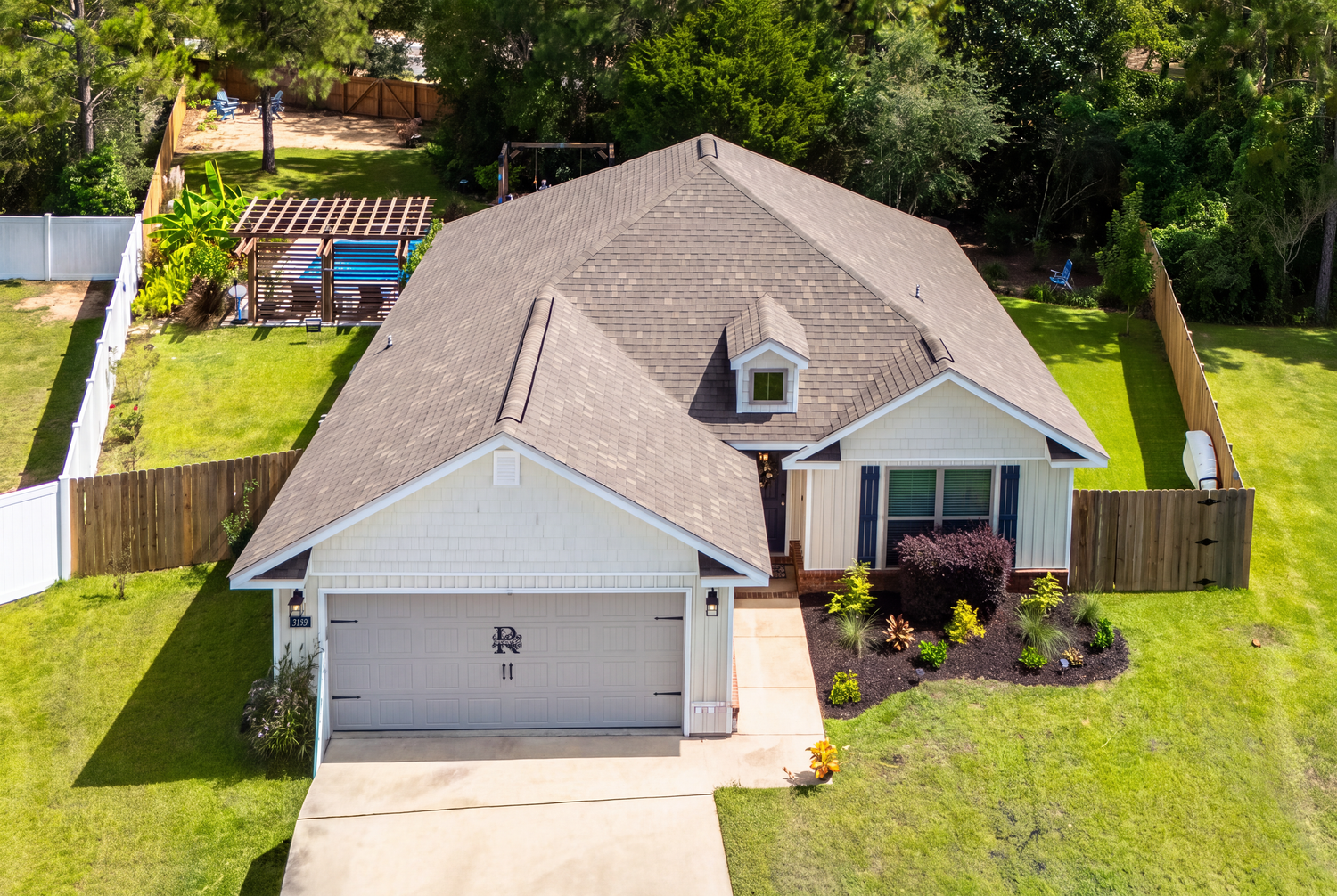 Aerial view of single-story home with gray roof, two-car garage, pool, and fenced yard.