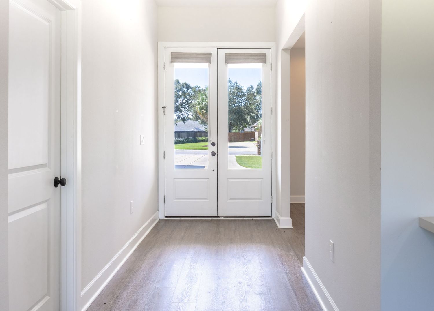 Bright entryway with white French doors, light hardwood floors, and white walls in a modern home.