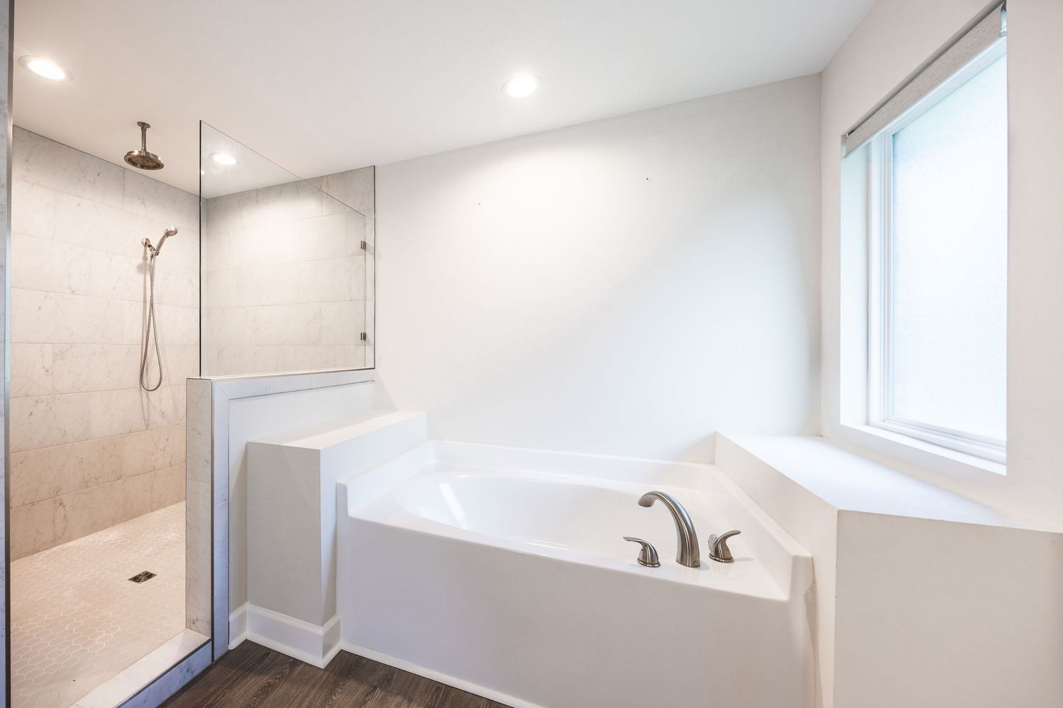 Modern bathroom with soaking tub, walk-in tiled shower, dark hardwood floors, and natural light from window.