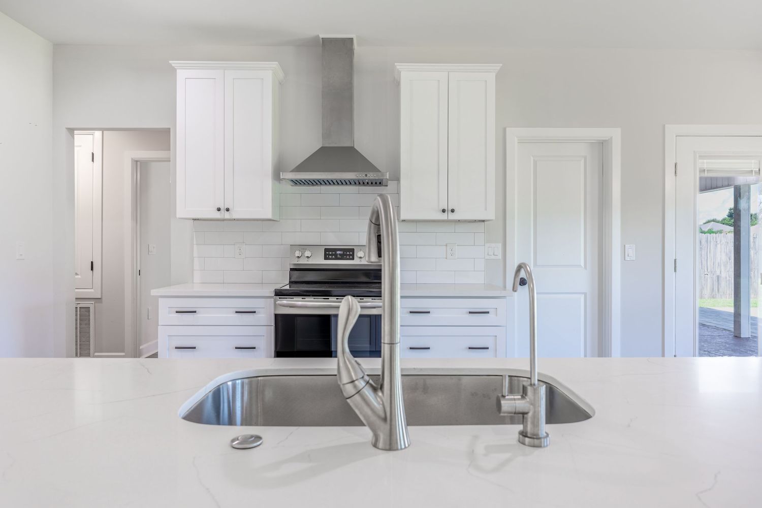 Modern white kitchen with stainless steel oven, range hood, subway tile backsplash, and quartz island with undermount sink.