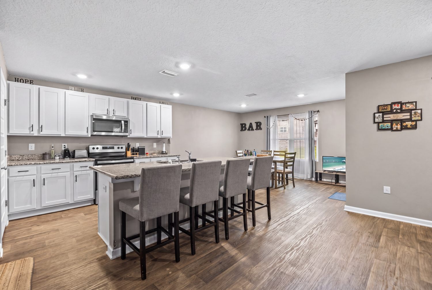 Modern kitchen with white cabinets, stainless steel appliances, gray island with bar seating, and open layout with hardwood floors.