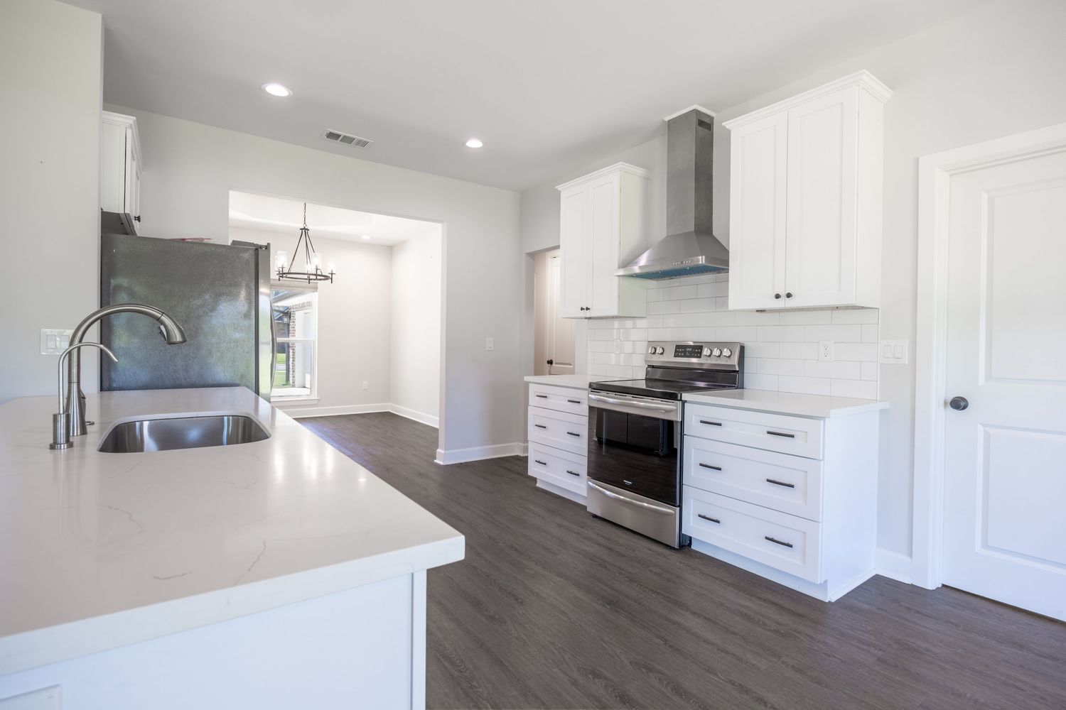 Modern white kitchen with stainless steel range, subway tile backsplash, dark hardwood floors, and quartz countertops.