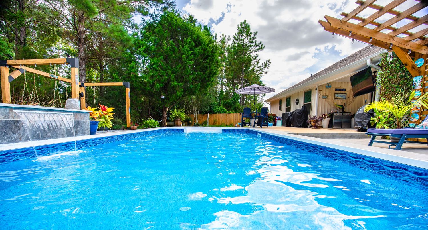 Stunning backyard pool with waterfall feature, pergola, and lush trees on a sunny day.