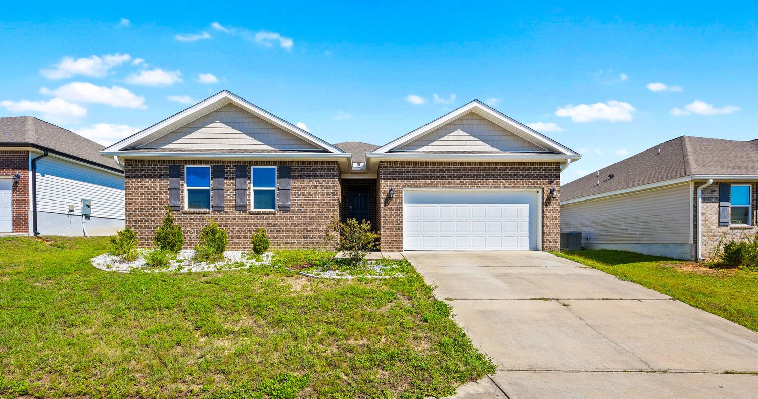 Charming brick ranch home with white garage door, manicured lawn, and decorative landscaping.