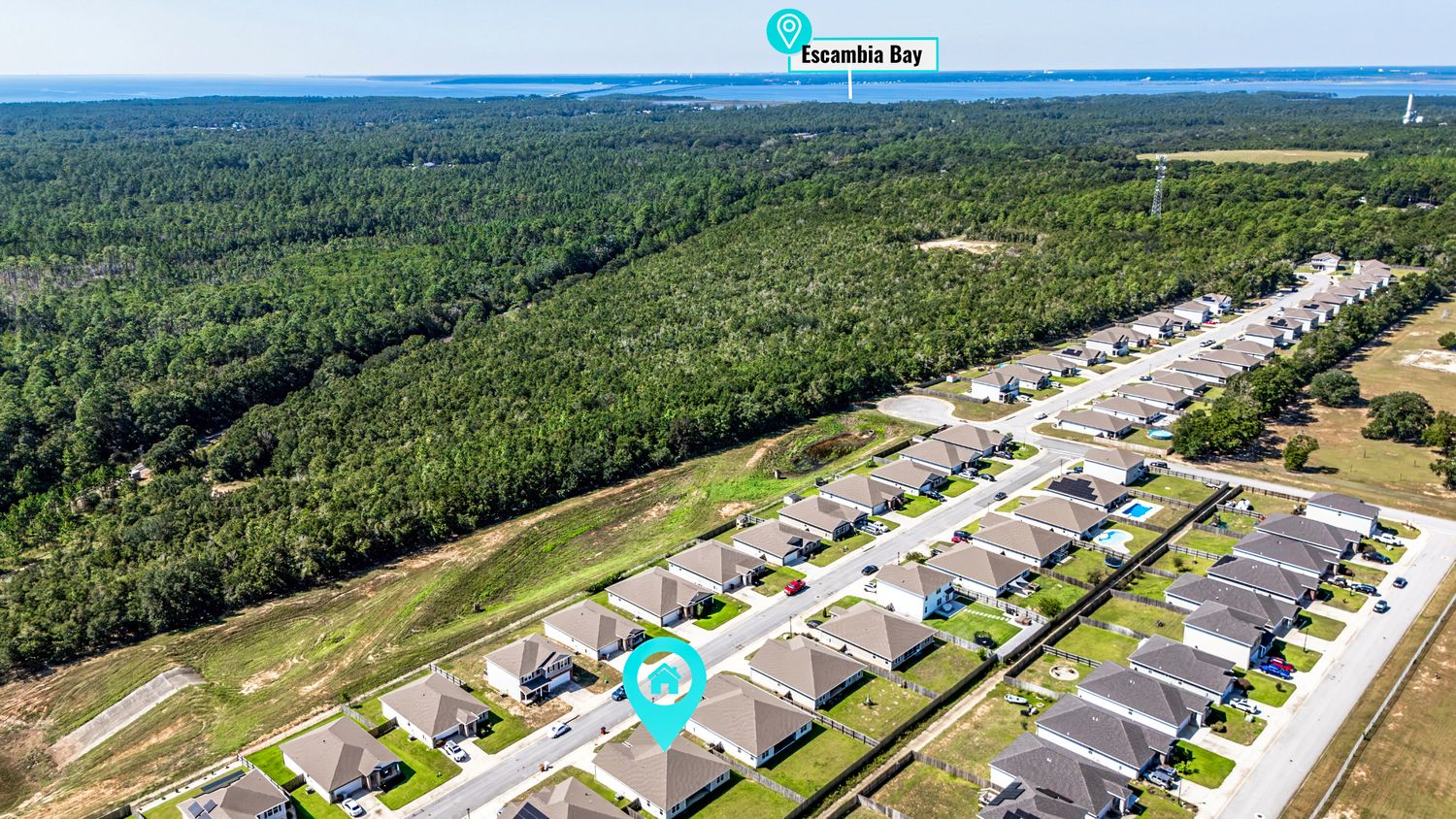 Aerial view of a residential neighborhood with rows of homes bordered by dense pine forest near Escambia Bay, Florida.