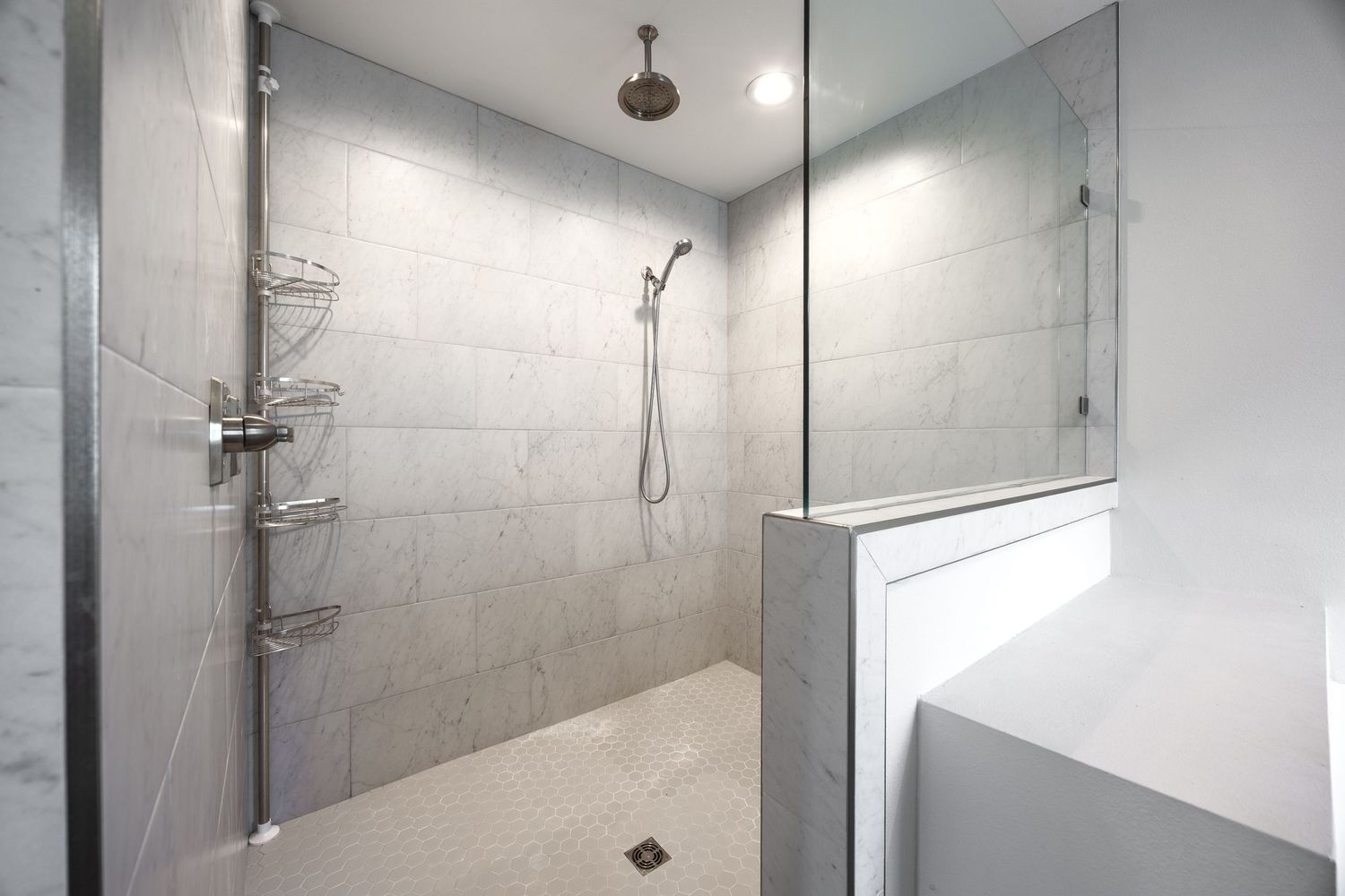 Spacious walk-in shower with marble tile walls, rain showerhead, glass partition, and built-in corner shelving.